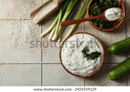 Delicious yogurt, green onion, cucumbers, parsley and salt on light tiled table, flat lay