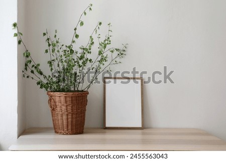 Spring, Easter still life. Elegant Scandinavian living room, home office. Empty vertical wooden picture frame mockup on desk, table. Wicker willow basket with green birch tree branches. Front view.