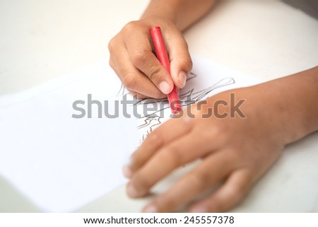 Child hand coloring on cartoon paper with color crayons