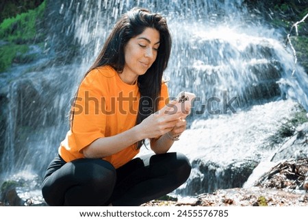Fit Woman Looking her phone in the spring mountain on a waterfall background 