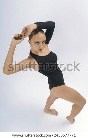 A young female dancer in a bodysuit shows elements of choreography with her hands above her head top view