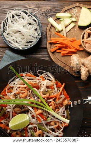 Shrimp stir fry with noodles and vegetables in wok on wooden table, flat lay