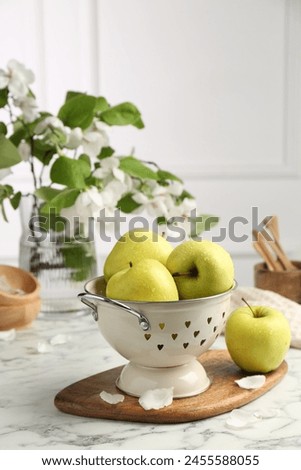 Colander with fresh apples and flower petals on white marble table