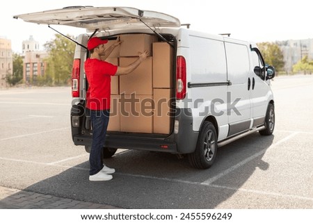 Courier man loading cardboard boxes to van, preparing for delivering postal parcel, outdoors shot Royalty-Free Stock Photo #2455596249