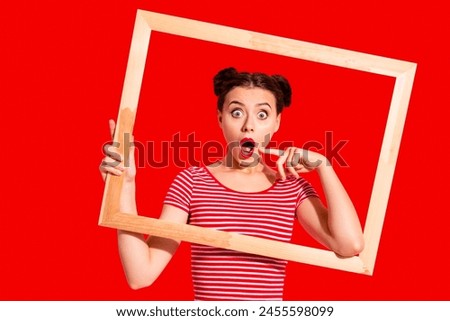 Portrait of her she nice cute charming attractive glamorous funny funky crazy girl in striped t-shirt holding in hands wooden frame posing opened mouth isolated on pink pastel background