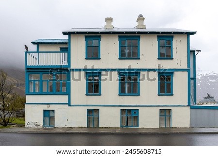 Traditional Icelandic white residential building with blue window frames, cladded in corrugated metal sheets in Seydisfjordur town in Iceland with foggy mountains in the background. Royalty-Free Stock Photo #2455608715