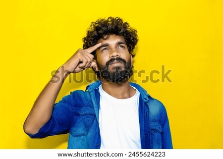 Confused preoccupied sad embarrassed upset young bearded Indian man wears a blue shirt looking aside think put a hand on his head have no idea isolated on a plain yellow background studio portrait Royalty-Free Stock Photo #2455624223
