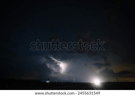 Dobele, Latvia - August 18, 2023 - Night sky with clouds and lightning, road lights, stars visible.