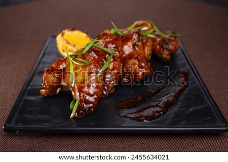 Grilled chicken wings in sweet tangy sauce with lemon slices. Perfect appetizer for a party or gathering. Delicious and flavorful dish. Royalty-Free Stock Photo #2455634021