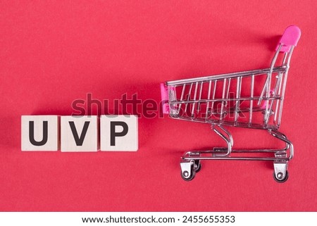 Wooden cubes building word UVP - (abbreviation Unique Value Proposition) on red background with mini shopping trolley