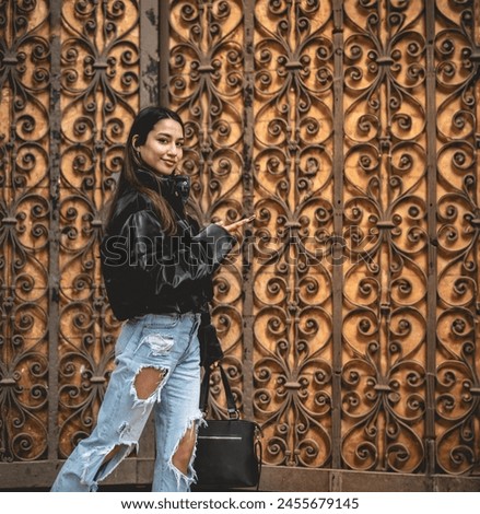 Stylish travel and urban exploration: vibrant young latina brunette with fashion look and pink suitcase exploring city downtown looking map on phone Royalty-Free Stock Photo #2455679145