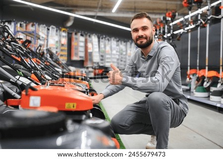 Young man buys a new lawnmower in a garden supplies store.