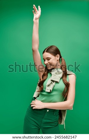A happy young beautiful girl in her 20s wearing a green shirt and green pants in a studio setting. Royalty-Free Stock Photo #2455682147