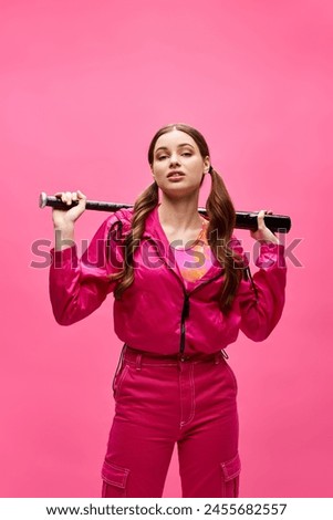 A stylish young woman in her 20s confidently holds a baseball bat against a vibrant pink background.