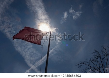 Red flag backlit by the sun with a blue sky for no entry to a shooting range. Royalty-Free Stock Photo #2455686803