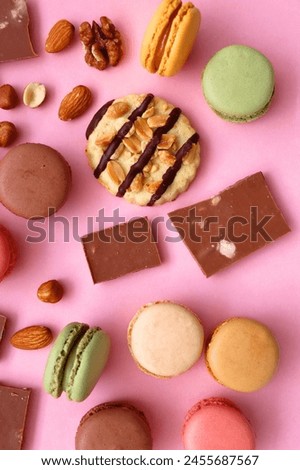 Pastel macarons, almond chocolate, peanut butter cookies and various nuts on bright pink background. Top view.