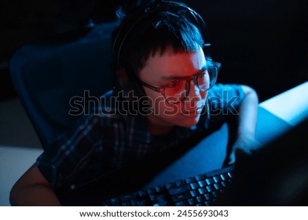 Young kid on the computer playing games, watching entertainment or browsing the online digital internet, young child raging, angry, focused and wearing glasses and dark background theme.
