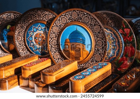 Uzbek wooden gift plates and caskets with wood carvings hand-painted asian patterns in the souvenir shop of Uzbekistan Royalty-Free Stock Photo #2455724599