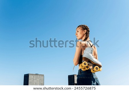Rear view of a young woman carrying her roller skates, urban background.
