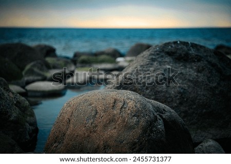 Dark ominous sea with sunset on the horizon in spring. Stones on the seashore. Soft selective focus. Artificially created grain for the picture
