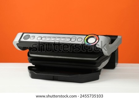 Electric grill on white wooden table against orange background, closeup. Cooking appliance