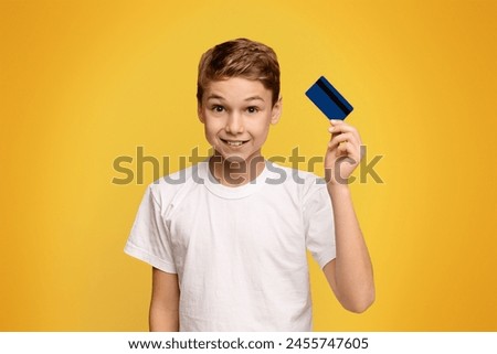 Kids banking. Cute boy holding credit card, orange studio background