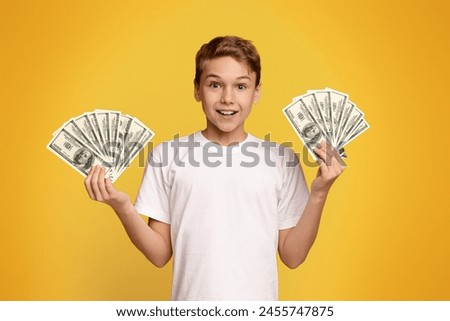 A young boy tightly grips two stacks of money in his hands, showing a sense of achievement and success.