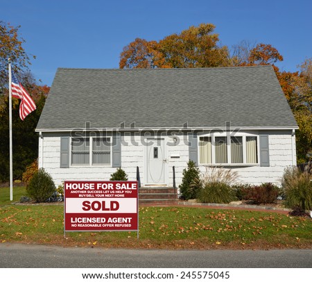 American flag pole Real estate sold (another success let us help you buy sell your next home ) sign front yard Suburban cape cod style home autumn day clear blue sky residential neighborhood USA