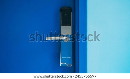 Close-up of a hotel room door featuring a stainless steel handle, electronic lock, and a blue Do Not Disturb sign.
