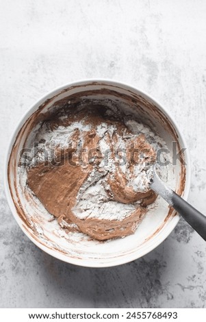 Chocolate cake batter being mixed in a white bowl, folding cake batter in a white mixing bowl, the process of making chocolate cake