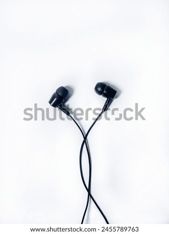 Black wired earphones. Wired earphones are tools commonly used for listening to audio and communicating 