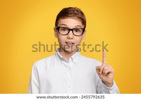 Little genius. Smart teen boy in glasses having idea, pointing his finger up, orange studio background Royalty-Free Stock Photo #2455792635