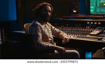 Sound engineer mixing and mastering tracks in professional recording studio, working with daw software and pushing sliders to adjust volume levels and edit audio recordings. Control room. Camera A.