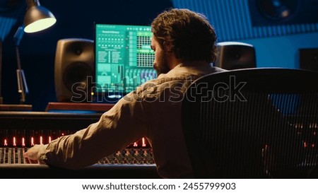 Sound designer mixing and mastering tracks on audio console in control room, using daw software on computer and editing files. Technician creating new music in professional studio. Camera A.