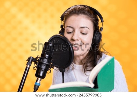 Smiling lady doing voiceover reading of book to produce audiobook. Happy voice actor using storytelling skills to entertain audience while producing digital recording of novel, studio background