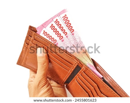 A man's hand holds a brown wallet containing 100,000 rupiah in cash.  Indonesian currency.