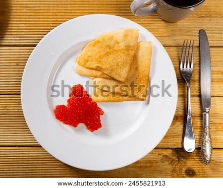 Pancakes with red caviar dished up in flat service plate. Traditional Russian cuisine Royalty-Free Stock Photo #2455821913