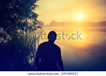 Man watching a sunrise over lake. Human silhouette