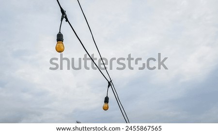 String lights hanging against a cloudy sky with a silhouette of tropical palm trees and distant mountains.