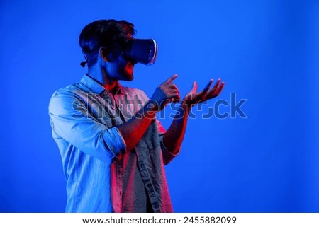 Caucasian smart man with VR glasses while holding hologram display in VR. Happy person holding and pointing while looking by using goggle and headset with neon light background. Technology. Deviation.