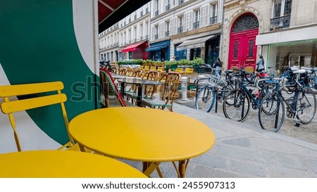 Colorful sidewalk cafe setting with yellow tables and chairs on a European city street, suggesting urban lifestyle and al fresco dining concepts Royalty-Free Stock Photo #2455907313