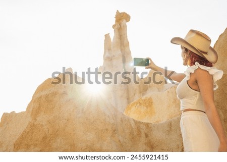 A woman in a cowboy hat is taking a picture of a mountain. The photo is in black and white