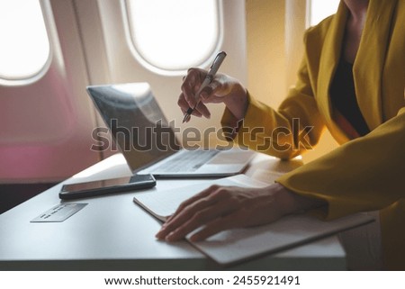 Attractive Asian businesswoman passenger sits on a business class luxury plane while taking notes on business, working with a tablet during a flight on an international trip. Royalty-Free Stock Photo #2455921491