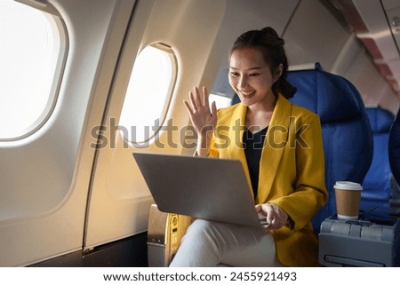 Young Asian business woman in yellow suit uses laptop sitting near window on airplane to do online financial business work Contact during flight, travel and business tourism concept.