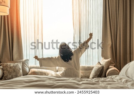 Hotel relaxation on lazy day with Asian woman waking up from good sleep on bed in weekend morning resting in comfort bedroom looking toward city view, having happy, work-life quality balance lifestyle Royalty-Free Stock Photo #2455925403