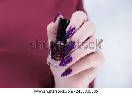 Woman hand with long nails and a bottle of plum purple nail polish