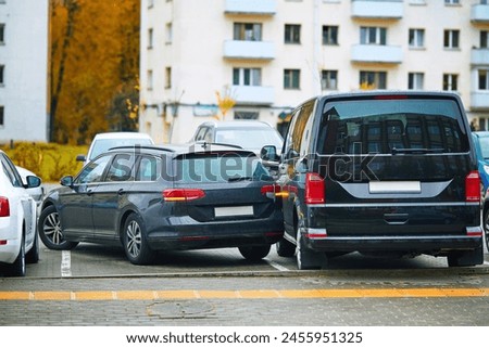 Car accident in tight parking lot, black sedan hitting parked van while backing up, reverse parking. Parking accident due to limited visibility, distracted driving. Rear-up collision. Minor accident Royalty-Free Stock Photo #2455951325