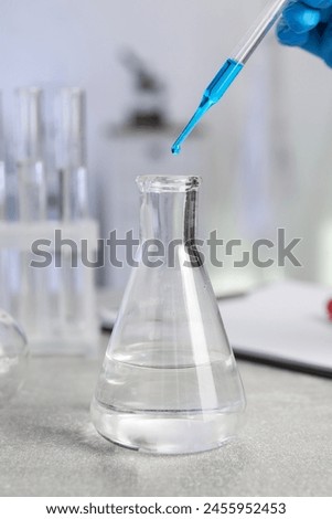 Laboratory analysis. Woman dripping liquid into flask at light grey table, closeup