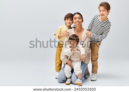 A young Asian mother and her children strike a pose in a studio against a grey background.