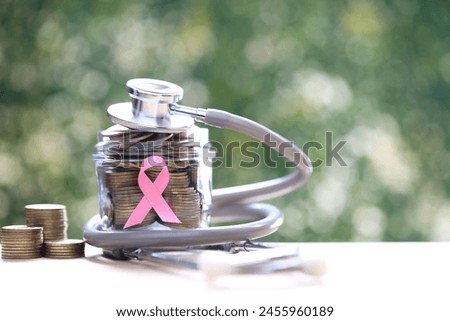 Symbol of breast cancer in women, Pink ribbon and coins money in glass bottle on green background, Healthcare and medicine concept